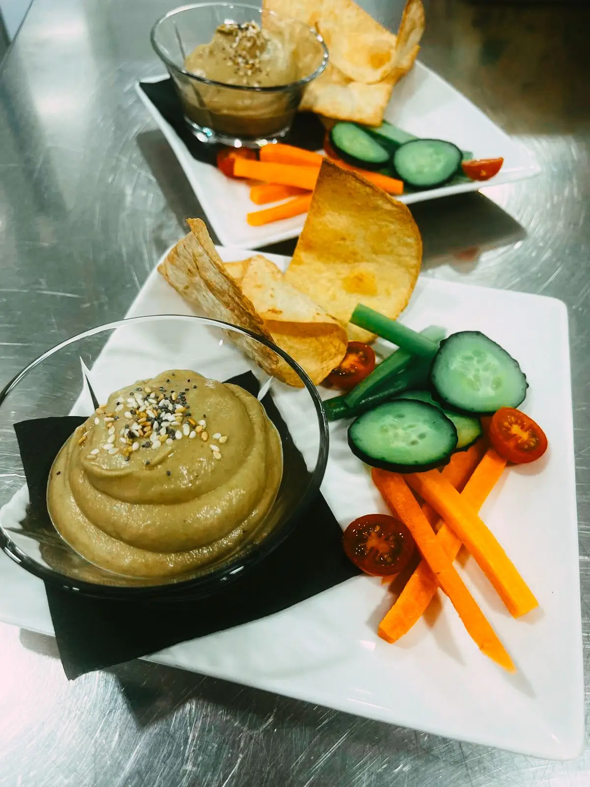 Dos platos de hummus con crudités de zanahoria, pepino, tomate cherry y chips en la cocina de Restaurante Rebeka en Barcelona