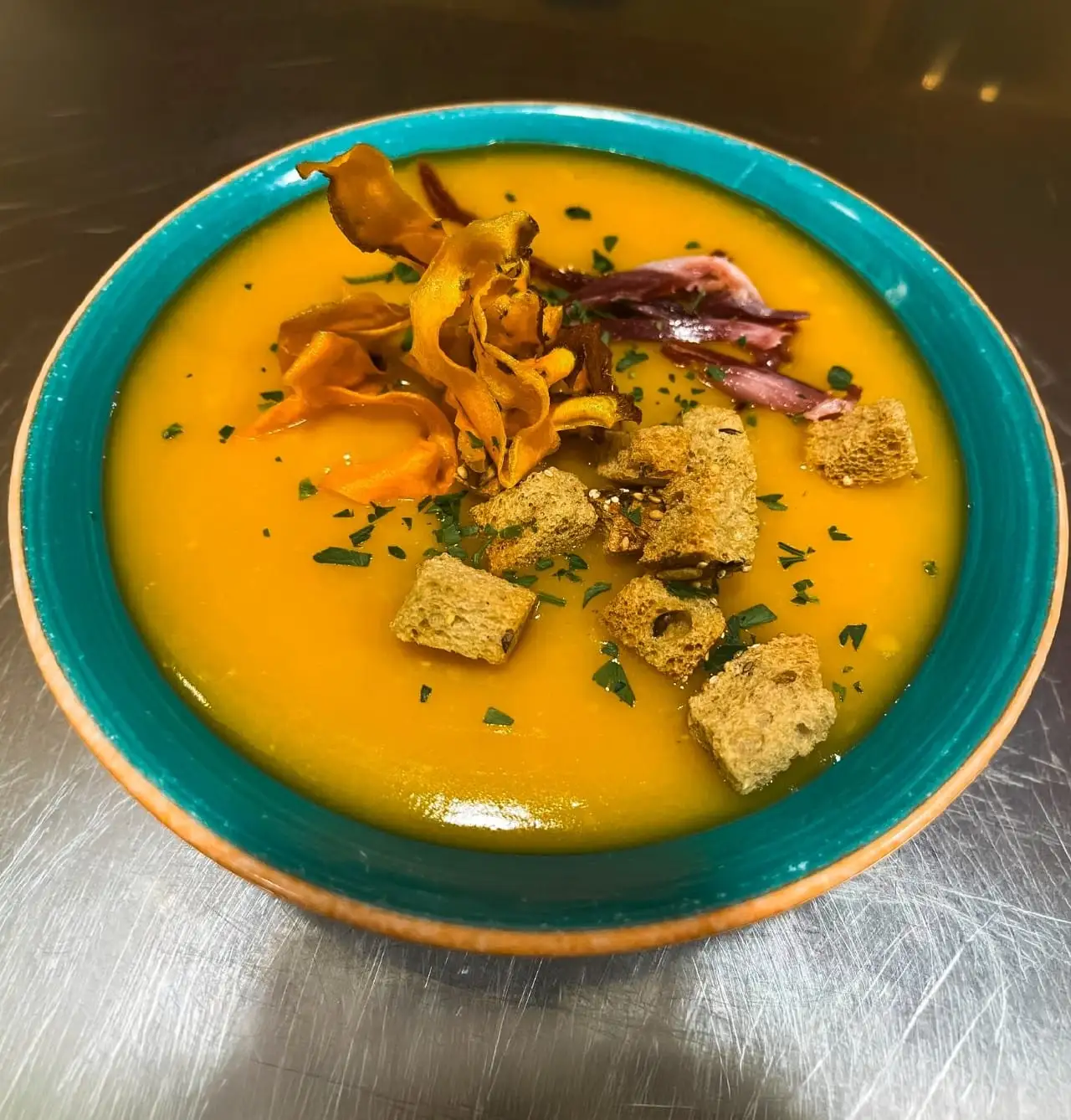 Crema de calabaza con picatostes y chips de verdura en plato hondo en Restaurante Rebeka, cerca de L’Auditori en Barcelona